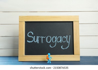 MYKOLAIV, UKRAINE - JANUARY 04, 2022: Small Blackboard With Word Surrogacy And Colorful Human Figures On Blue Wooden Table