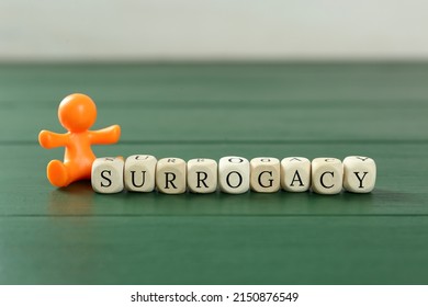 MYKOLAIV, UKRAINE - JANUARY 04, 2022: Cubes With Word Surrogacy And Baby Figure On Green Wooden Table, Closeup