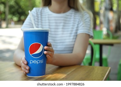 MYKOLAIV, UKRAINE - JUNE 9, 2021: Woman With Paper Pepsi Cup At Wooden Table In Outdoor Cafe, Closeup