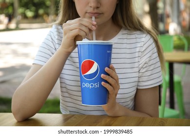 MYKOLAIV, UKRAINE - JUNE 9, 2021: Woman Drinking Pepsi From Paper Cup At Table In Outdoor Cafe, Closeup