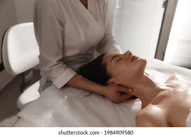 Myofascial massage and body care. Woman relaxing on therapy table at beauty salon, cosmetology clinic, massagist rubbing clients neck to reduce pain and tension of muscles