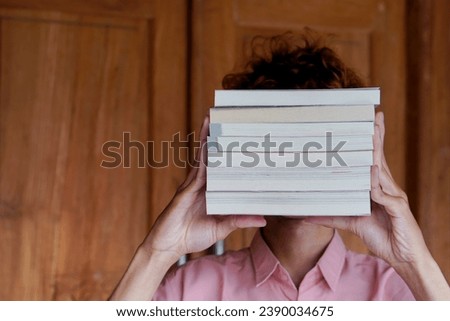 Mysterious Asian man covering his face with a stack of books. Education and knowledge concept. Portrait of young male book lover
