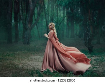A mysterious blonde girl in a long pink dress with a train and a raincoat that flutters in the wind. The wizard leaves in a forest covered with fog. A background of trees with a haze away. Art photo