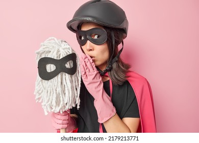 Mysterious Dark Haired Woman Whispers Secret To Washing Mop Dressed Like Superhero Ready To Clean Your House Shares Confidential Information Isolated Over Pink Background. Housekeeping Concept