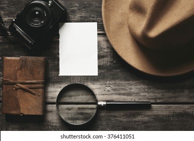 Mysterious detective game concept notebook leather cover sheet white paper felt brown hat portable mirrorless microthird digital photo camera big vintage magnifier isolated on black aged wood table - Shutterstock ID 376411051