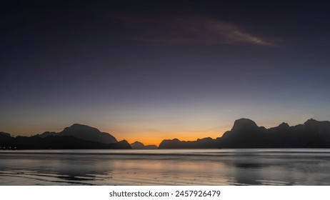 A mysterious evening after sunset on a tropical island. Silhouettes of mountains against the  purple sky illuminated by orange at the horizon. Reflection on the calm surface of the ocean. Philippines. - Powered by Shutterstock