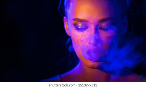 Mysterious girl smoking e-cigarette in neon blue and orange light, copy space