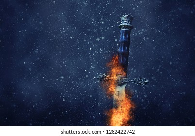 mysterious and magical photo of silver sword with fire flames over Gothic snowy black background. Medieval period concept