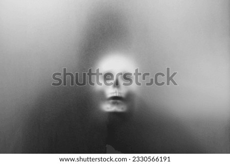 Mysterious man holding a skull in his hand standing behind frosted glass looking mysterious and scary looking like a sorcerer.haunting concept.halloween concept.