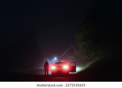 A mysterious man standing next to a car on a spooky empty road on a foggy night. Silhouetted by street lights. - Powered by Shutterstock