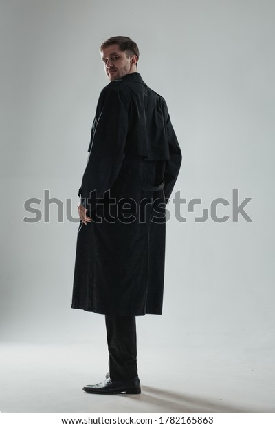 Mysterious man turned back to camera in a long\
dark trench coat. Vertical\
image.