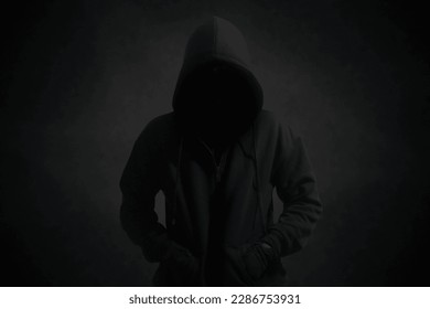 Mysterious man wearing black hoodie standing against dark background. Hacker, crime, and cyber security concept. - Powered by Shutterstock