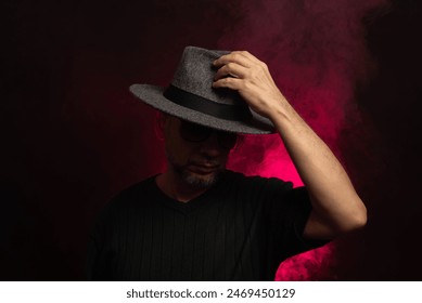 Mysterious, middle-aged man wearing gray hat. Isolated on studio artificial smoke filled background with red rose color. - Powered by Shutterstock