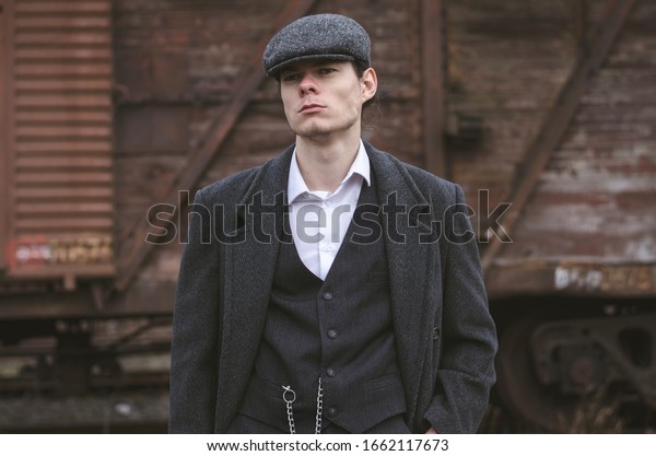Mysterious portrait of retro 1920s english\
gangster with flat cap on railway\
station.	