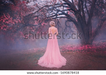 Mysterious silhouette princess. young blonde woman queen turned away. backdrop autumn nature mystic blue fog pink full bloom fairy tree black trunk. spring pink long elegant vintage dress bare back