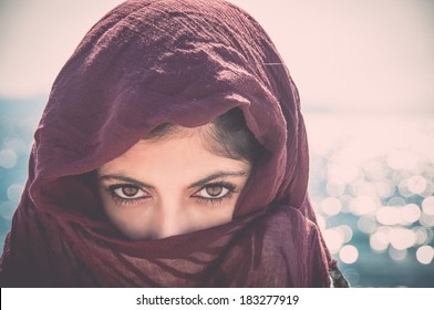 mysterious woman with her face covered and only her eyes showing with a vintage filter applied
