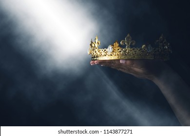 mysteriousand magical image of woman's hand holding a gold crown over gothic black background. Medieval period concept - Shutterstock ID 1143877271
