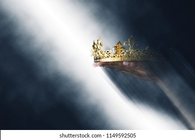 mysteriousand magical image of woman's hand holding a gold crown over gothic black background. Medieval period concept - Shutterstock ID 1149592505