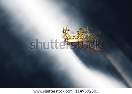 mysteriousand magical image of woman's hand holding a gold crown over gothic black background. Medieval period concept