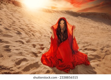 Mystery arabic woman sits in desert, gold mask veil accessories niqab burqa hide face. Fantasy girl art photo fashion model black hair head cover scarf, red long dress. Sand dunes sun light