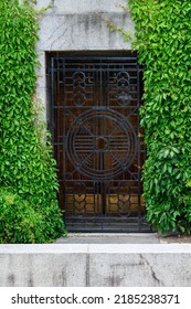 Mystery Garden, Black Metal Grate Door In A Cement Wall Covered In Green Vines, As A Nature Background
