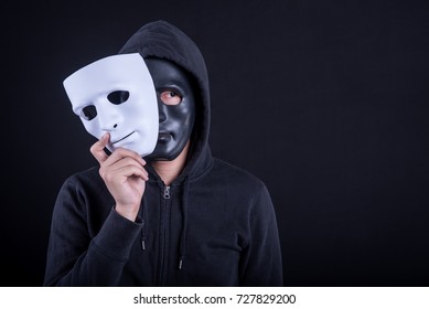 Mystery man wearing black mask holding white mask. Anonymous social masking or halloween concept.