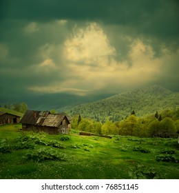 Mystery mountain landscape. Ray of light in dark clouds over the old wooden shack in green valley