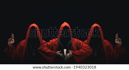 Mystery people in a red hooded cloaks in the dark. Hiding face in shadow. Pointing up with fingers. Satanic symbols. Ghostly figure.