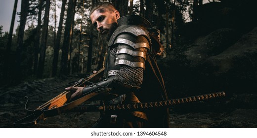 Mystery scarface knight in armor with sword and crossbow in the forest