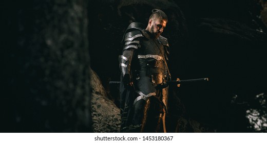 Mystery scarface knight in armor with sword and crossbow in the forest