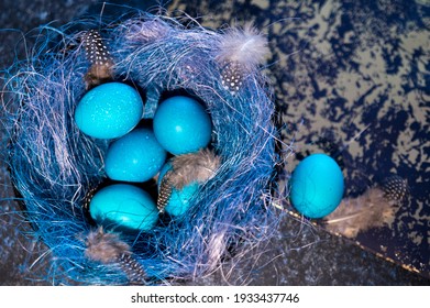 Mystical coloring Easter eggs with twigs in a decorative nest on blue background. Background with copy space. Selective focus