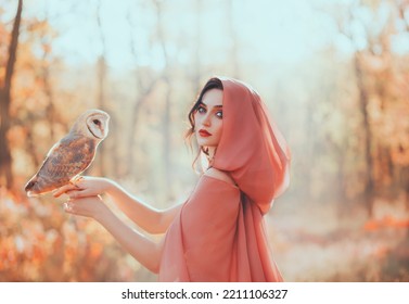 Mystical Fantasy Woman Walks In Autumn Orange Forest, Holds Cute Pet Bird Little Barn Owl On Hand. Girl Princess. Medieval Old Style Clothig Cape Hood Peach Dress. Bright Make-up Red Lips Pale Skin