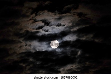Mystical landscape with white full moon in the night sky obscured by cumulus clouds - Shutterstock ID 1857890002
