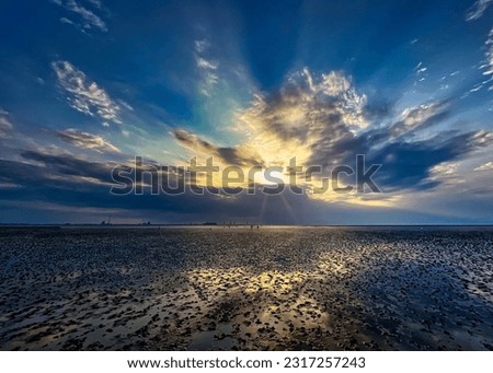 Mystical sunset on the North Sea: Captured during low tide in the mudflats of Tossens Beach, Butjadingen, an enchanting spectacle unfolds as the sun dips below the horizon.