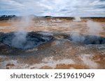 Myvatn Iceland, view across colourful landscape with mud pools and steam vents at Namafjall or Hverir geothermal area with car park in background
