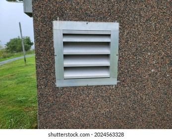 n air vent in the exterior of a suburban home. The vent has several slats for air to pass through. It's in the cement foundation of the house.