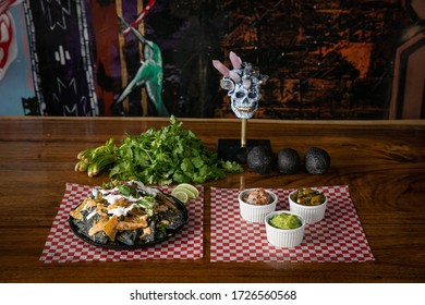 Nacho Platter With Fresh Ingredients, Guacamole And Sauces. Skull Sculpture In Background