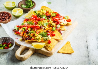 Nachos chips with cheese sauce, guacamole, salsa and vegetables on the board. Party food concept. Mexican food concept.