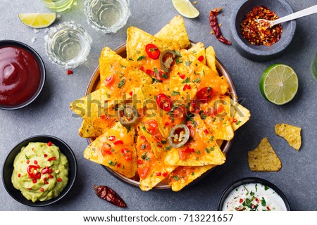 Nachos chips with melted cheese and dips variety in black bowl. Top view.