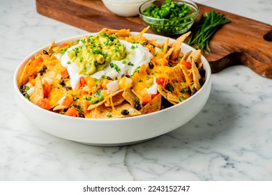 Nachos. Crispy tortilla chips topped with melted cheddar cheese, salsa, black beans, jalapenos, guacamole, sour cream and lettuce. Tex-Mex or Mexican restaurant classic traditional menu item. 