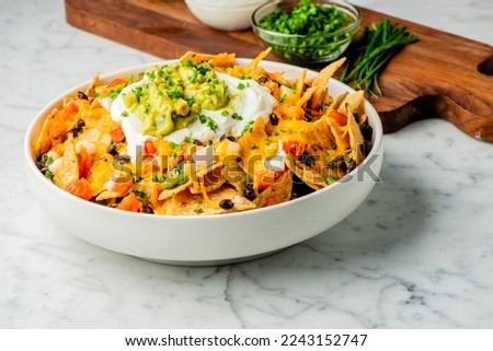 Nachos. Crispy tortilla chips topped with melted cheddar cheese, salsa, black beans, jalapenos, guacamole, sour cream and lettuce. Tex-Mex or Mexican restaurant classic traditional menu item. 