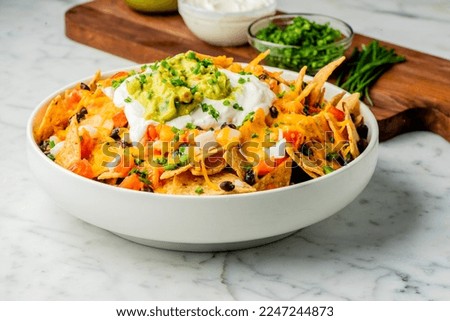 Nachos. Crispy tortilla chips topped with melted cheddar cheese, salsa, black beans, jalapenos, guacamole, sour cream and lettuce. Tex-Mex or Mexican restaurant classic traditional menu item. 