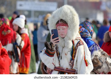 Nadym, RUSSLAND-MÄRZ 13, 2022: Nenets Rentiermädchen in Pelzbekleidung spricht am Telefon während des traditionellen Feiertags Reinirder Herder's Day