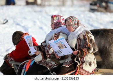 Nadym, RUSSLAND-MÄRZ 13, 2022: Nenets Women Rentierzüchter in nationalen Kleidungsstücken lesen die regionale Presse während des traditionellen Feiertags des Rentierertags
