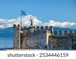 Nafpaktos port castle, with the statue of Georgios Anemogiannis, a hero of the Greek Independence War (1821), and a Greek flag waving, in Nafpaktos city, Etoloakarnania region, Greece, Europe.