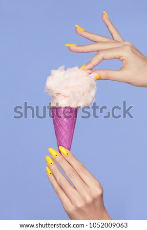 Nail Art. Hands With Colorful Nails And Cotton Sugar Ice Cream. Closeup Of Female Hands With Trendy Orange Manicure Holding Cone With Cotton Candy On Purple Background. Nail Design. High Quality
