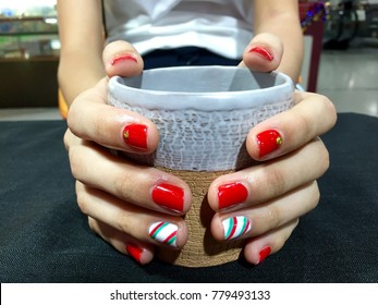 Nail artist. Female hands with red and christmas candy canes on nail. Christmas and happy holiday concept. Close-up of a woman is holding a cup of coffee.