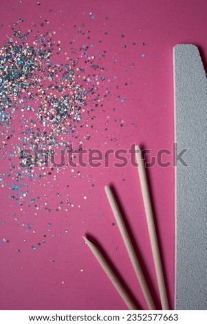 Nail file, wooden sticks and a brush for manicure on a pink background with sparkles 