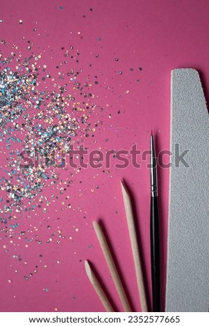 Nail file, wooden sticks and a brush for manicure on a pink background with sparkles 