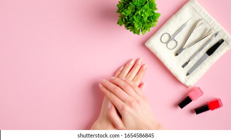 Nail Salon Table With Manicure Tools, Nail Polish Bottles And Female Hands On Pink Background. Nail Studio Workspace Concept